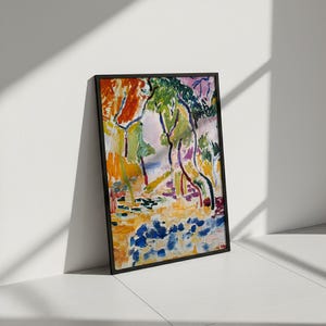 May include: A framed abstract landscape painting with a black frame. The artwork features vibrant colors, including orange, green, blue, and purple, depicting trees and foliage. The painting is leaning against a white wall.
