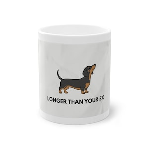 Könnte beinhalten: Weiße Keramiktasse mit einer Illustration eines schwarz-braunen Dackels und dem Text "LONGER THAN YOUR EX". Der Hund blickt nach oben. Die Tasse hat einen hellgrauen Hintergrund.