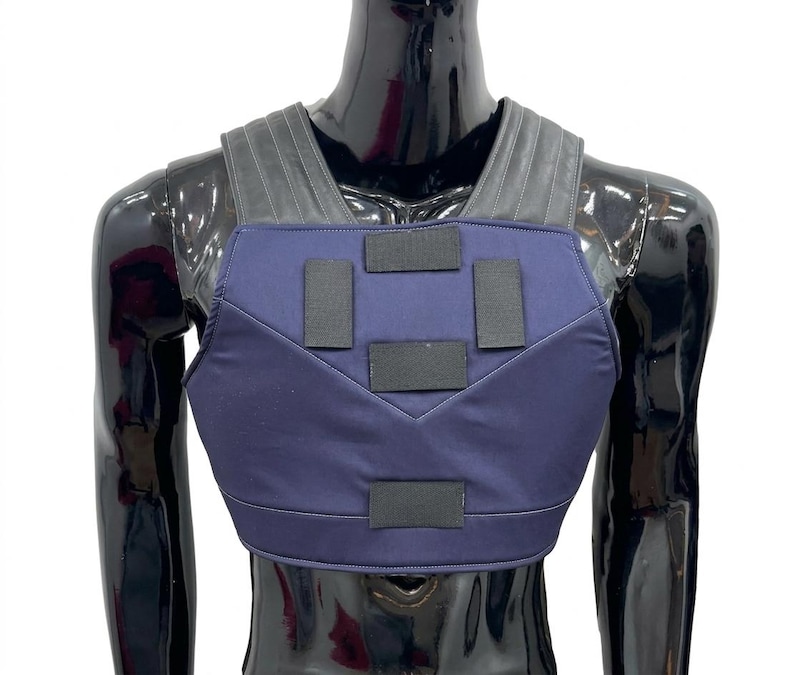 May include: A dark blue chest protector vest featuring five rectangular black hook-and-loop fastener patches on the front panel and wide, ribbed black shoulder straps that extend over the upper torso area for a secure fit.
