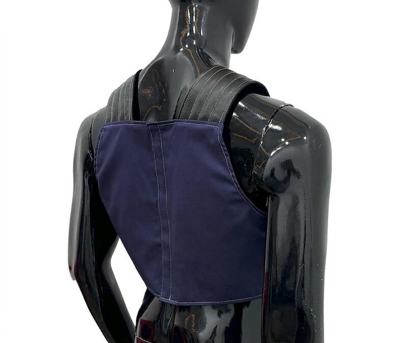 May include: A navy blue vest featuring a structured design with wide black shoulder straps. The garment is constructed with visible vertical stitching along the center back panel and across the shoulder straps, providing a clean, tailored appearance.