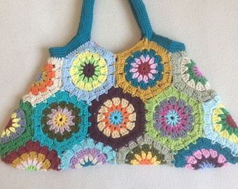 May include: A crocheted tote bag with a teal handle and a colorful patchwork design of multi-colored granny squares.