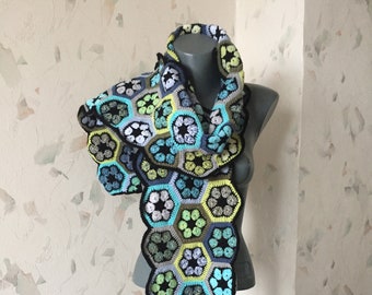 May include: A long, crocheted scarf with a geometric pattern of hexagons in shades of green, blue, black, and gray.
