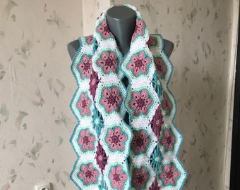 May include: A crocheted scarf with a floral pattern in shades of white, pink, green, and blue. The scarf is displayed on a wooden mannequin.