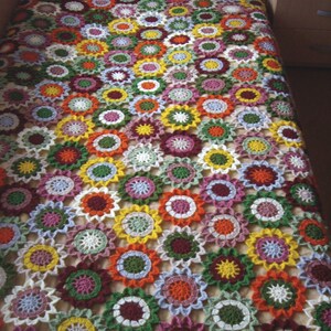 May include: A crocheted blanket with a floral pattern in shades of white, green, red, orange, yellow, and pink.