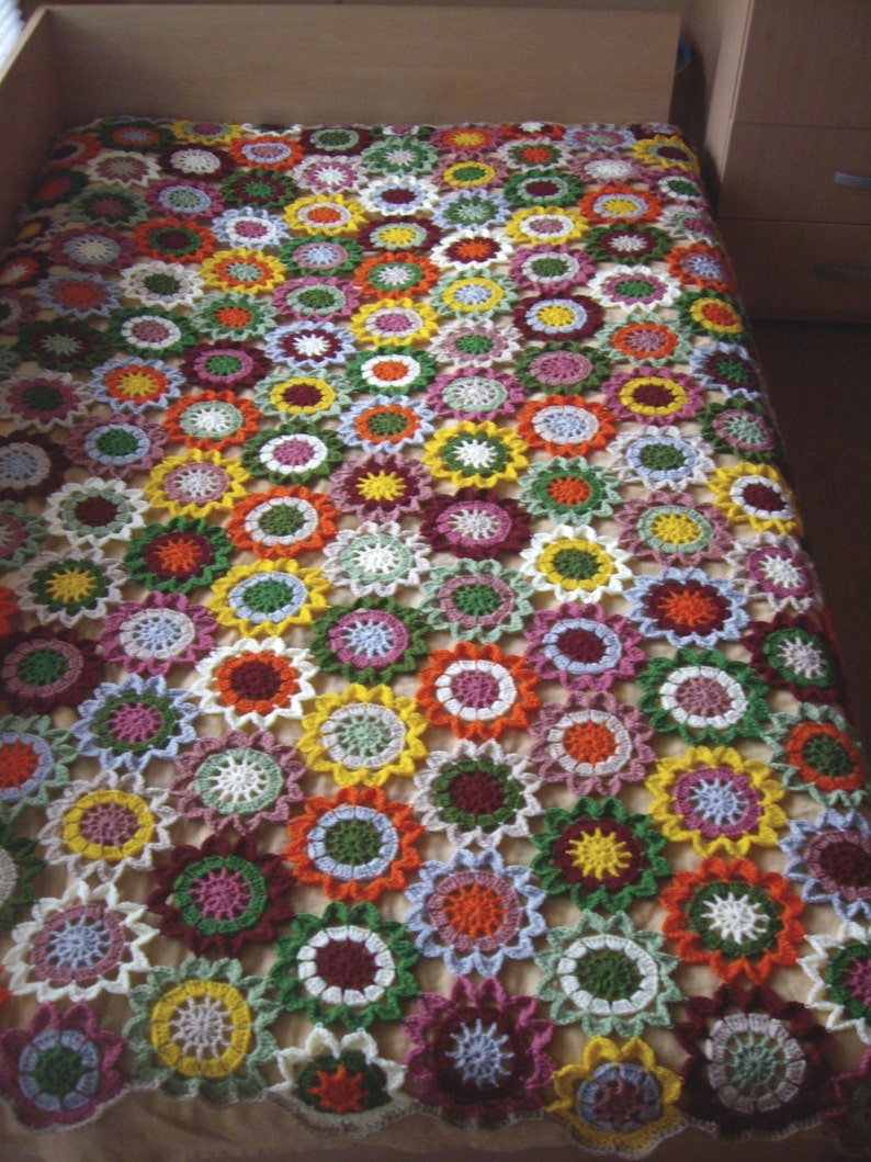May include: A crocheted blanket with a floral pattern in shades of white, green, red, orange, yellow, and pink.