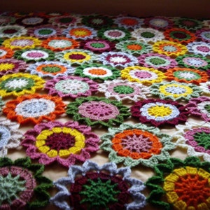 May include: A colorful crocheted blanket with a floral pattern. The blanket is made up of many different colored squares, each with a different flower design. The blanket is perfect for adding a touch of color and warmth to any room.