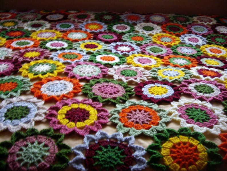 May include: A colorful crocheted blanket with a floral pattern. The blanket is made up of many different colored squares, each with a different flower design. The blanket is perfect for adding a touch of color and warmth to any room.