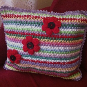 May include: A colorful striped crocheted pillow with three red fabric flowers. The flowers have black button centers.