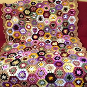 May include: A crocheted blanket with a hexagonal pattern in shades of brown, pink, yellow, green, purple, and white.