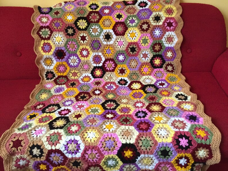 May include: A crocheted blanket with a hexagonal pattern in shades of brown, pink, yellow, green, purple, and white.