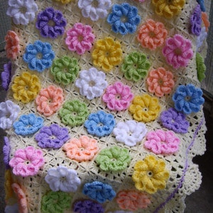 May include: A crocheted baby blanket with a yellow background and colorful flower designs. The blanket has a white crocheted border with a purple edging.