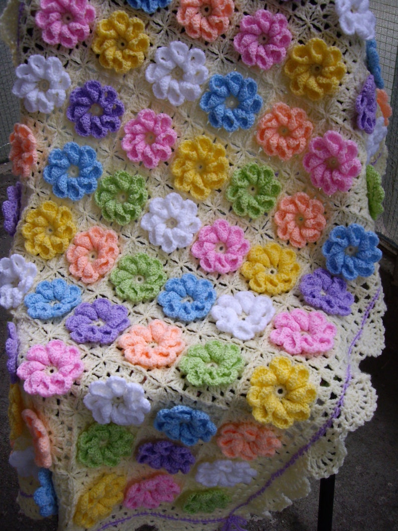 May include: A crocheted baby blanket with a yellow background and colorful flower designs. The blanket has a white crocheted border with a purple edging.