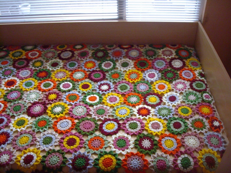 May include: A crocheted blanket made of colorful flower-shaped motifs. The blanket is made with a variety of colors, including red, orange, yellow, green, blue, and purple.