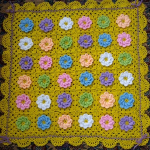 May include: A yellow crocheted baby blanket with a scalloped border. The blanket is made up of squares with different colored flowers in each square. The flowers are in shades of pink, purple, blue, green, and white.