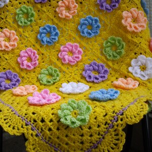 May include: A yellow crocheted baby blanket with a purple border and colorful flower accents.
