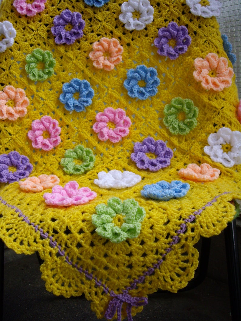 May include: A yellow crocheted baby blanket with a purple border and colorful flower accents.