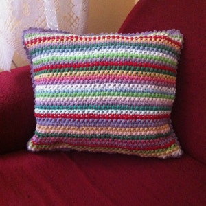May include: A colorful striped pillow with a crocheted design. The pillow is made with a variety of colors, including red, green, purple, and white.