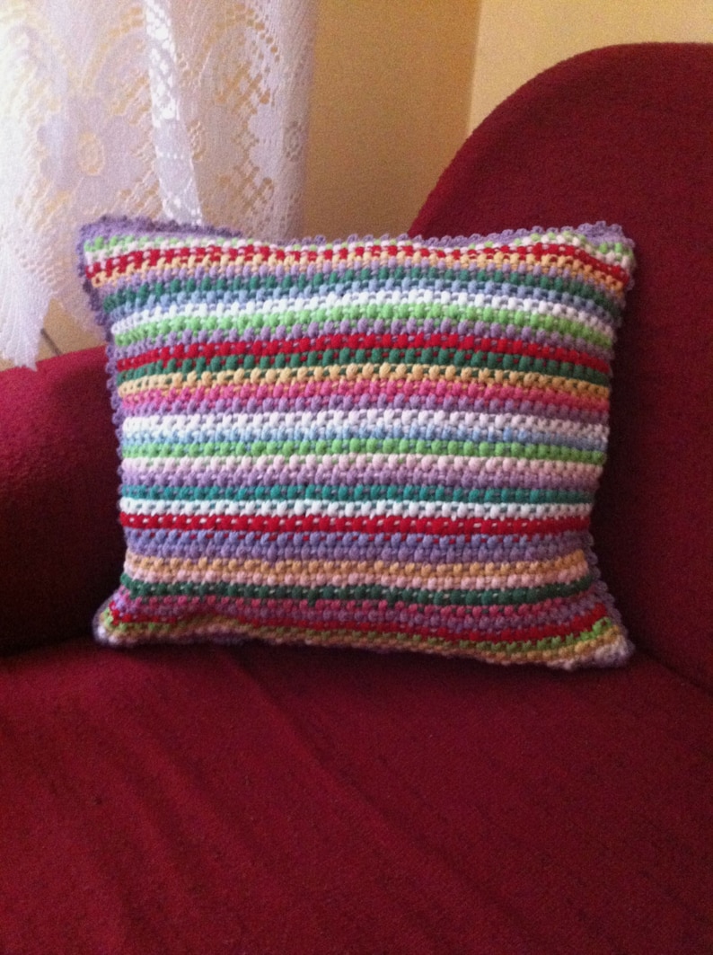 May include: A colorful striped pillow with a crocheted design. The pillow is made with a variety of colors, including red, green, purple, and white.