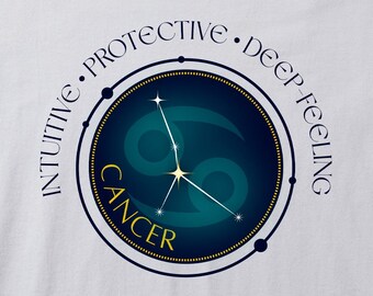 May include: White t-shirt featuring a Cancer zodiac design. The design includes the Cancer symbol in teal and gold, with a constellation and the word "CANCER". The words "INTUITIVE", "PROTECTIVE", and "DEEP-FEELING" are arched around the circle.