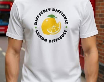 May include: White t-shirt with a graphic of a yellow lemon and a lemon slice. The text around the lemon reads "DIFFICULT LEMON DIFFICULT" in a circular pattern. The shirt is short-sleeved.