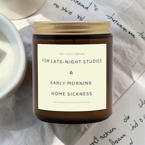 May include: A white ceramic mug with a black handle and the text "But First, Coffee" in a bold, black font. The mug is set against a blurred background, highlighting its clean design.