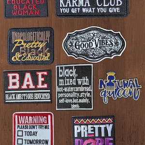 May include: A collection of nine rectangular and shaped embroidered patches featuring various text designs including WARNING EDUCATED BLACK WOMAN, KARMA CLUB, UNAPOLOGETICALLY PRETTY BLACK & EDUCATED, GOOD VIBES, BAE, and other phrases in black, white, red, gold, and purple.