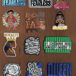 May include: A collection of twelve embroidered patches featuring various designs including text such as She Is Fearless, Brown Sugar Babe, I Am A Go Getter, Royalty, My Family My Greatest Treasure, F*** Around And Find Out, Give Me My Roses While I'm Here, and Queen, alongside illustrations of characters, a rose, and a game board.