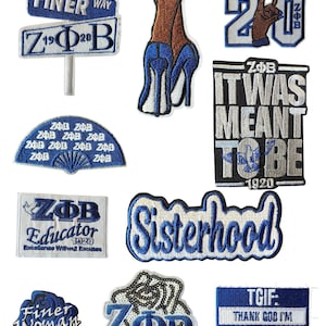 Peut inclure: Plusieurs écussons brodés bleus et blancs. Les motifs comprennent des textes tels que "Sisterhood", "Finer Woman" et "TGIF: Thank God I'm Finer". D'autres écussons présentent les lettres ZΦB et le chiffre 1920.