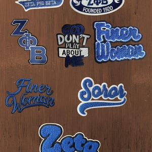 Può includere: Una collezione di toppe ricamate con disegni blu e bianchi legati a Zeta Phi Beta. Le toppe includono testi come Legacy, Zeta Phi Beta Founded 1920, Z Phi B, God Don't Play About Me, Finer Woman, Soror e Zeta in vari caratteri tipografici.