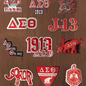 May include: A collection of eleven embroidered patches in red, white, and black featuring Greek letters Delta Sigma Theta, the year 1913, elephant silhouettes, and text including It's In My DNA, Sisterhood, Nineteen 13, J-13, All Eyes On Me, and Soror.