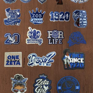 Op de afbeelding: Een verzameling geborduurde patches met blauw-witte ontwerpen gerelateerd aan de Zeta Phi Beta sorority. De patches bevatten diverse logo's, teksten zoals 1920, Finer en Sisterhood, samen met afbeeldingen van duiven, kronen, rozen en figuren.