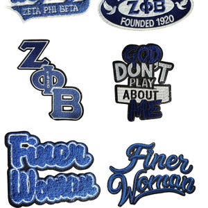 May include: Embroidered patches in shades of blue and white. The patches feature text such as "Legacy," "Zeta Phi Beta," "God Don't Play About Me," and "Finer Woman." Some patches have an oval shape.