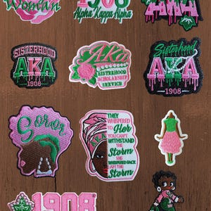 May include: A collection of eleven embroidered patches featuring pink and green colour schemes, including text such as Pretty Woman, 1908, Alpha Kappa Alpha, AKA, Sisterhood, Scholarship, Service, and They whispered to her you can't withstand the storm.