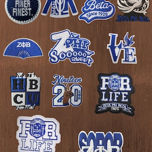 Op de afbeelding: Een collectie van twaalf geborduurde patches in blauw en wit, met thema's van de Zeta Phi Beta studentenvereniging. De ontwerpen bevatten teksten zoals Fine Finer Finest, Zeta Phi Beta Since 1920, For Life en diverse logo's, symbolen en handgebaren.