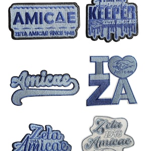 May include: A selection of blue and white embroidered patches. The patches display the words "AMICAE", "I Z A", "Zeta Amicae", and "I AM MY FRIENDS KEEPER". Some patches include the text "ZETA AMICAE SINCE 1948" and "Zeta 1948 Amicae".