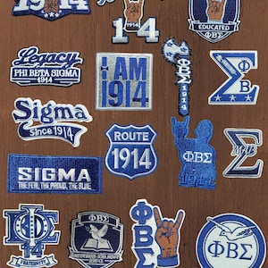 May include: A collection of embroidered patches featuring blue and white Phi Beta Sigma fraternity designs, including text like 1914, Legacy, Sigma, Route 1914, and I AM 1914, along with symbols like hands making a sign, a dove, and Greek letters.