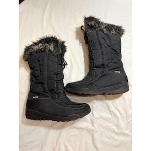 May include: A pair of black winter boots with faux fur trim at the top. The boots have a quilted design, a lace-up closure, and a red sole. The boots are designed for cold weather and snow.