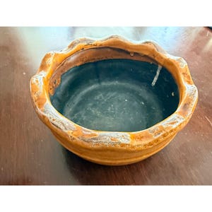 May include: A ceramic bowl with a scalloped rim. The bowl has a dark interior and a light brown exterior with a darker brown rim. The bowl is likely used for serving or display.