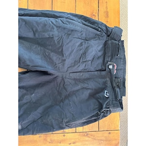May include: Black snow pants with multiple pockets and a belt. The pants are made of a durable, water-resistant material. The pants are designed for winter sports and outdoor activities.