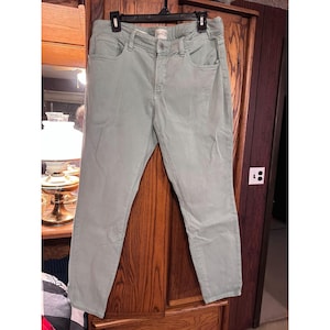 May include: Light green women's jeans hanging on a black hanger. The jeans have a button and zipper closure, with pockets on the front and back. The pants are made of a soft, durable material.