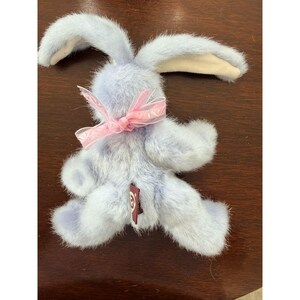 May include: A plush lavender bunny with long ears and a pink ribbon bow around its neck. The stuffed animal has a soft, furry texture and a small tag on its rear. A cute Easter or spring-themed gift.