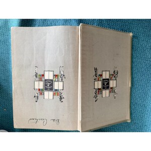May include: An open book with light gray pages. The cover and inside pages feature a decorative emblem with the words "Modern Library" and illustrations of figures and books. The book is open to reveal the title page.