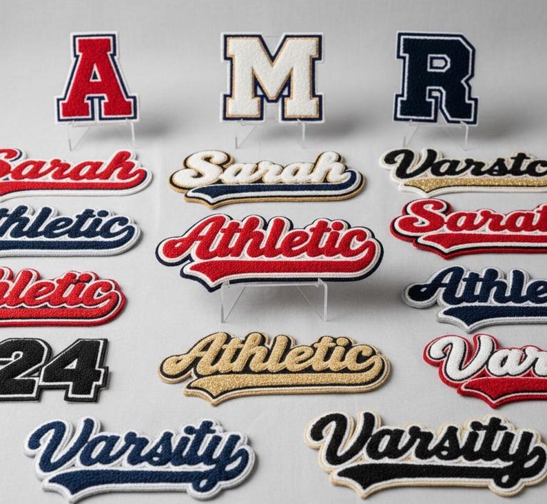 Puede incluir: Surtido de parches universitarios bordados en varios colores y dise&ntilde;os. Incluye letras, nombres y la palabra "Athletic" en rojo, azul y dorado. Los parches se muestran sobre soportes transparentes sobre un fondo claro.