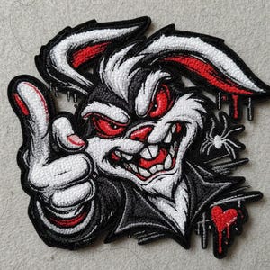 May include: Embroidered patch featuring a menacing rabbit with red eyes and a sinister grin. The rabbit gives a thumbs-up, with a dripping heart and spider adding to the edgy design. The patch is black, white, and red.