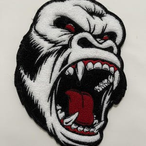 Puede incluir: Parche bordado con la cabeza de un gorila con la boca abierta, mostrando afilados dientes blancos y una lengua roja. La cara del gorila es blanca con contornos negros y ojos rojos. Ideal para ropa o complementos.