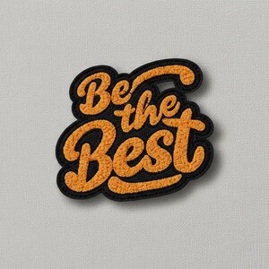 Op de afbeelding: Een zwart en oranje geborduurd embleem met de tekst "Be the Best" in een retro lettertype. De tekst is oranje met een fuzzy textuur, omlijnd in zwart. Het embleem heeft een zwarte rand en een neutrale achtergrond.