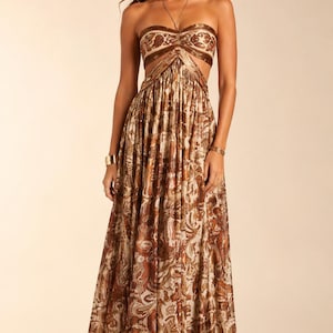 May include: A floor-length strapless maxi dress featuring a brown and cream paisley print. The garment includes a fitted bodice with cut-out details at the waist and a flowing, pleated skirt that extends to the floor in a continuous pattern.