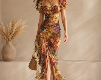 May include: A floral print maxi dress with a thigh-high slit. The dress features a square neckline, short puff sleeves, and a ruffled bodice. The color palette includes shades of yellow, orange, purple, and brown. The model is wearing brown sandals and carrying a woven bag.