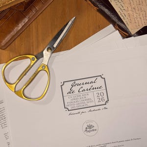Peut inclure: Ciseaux à poignée dorée et lames argentées posés sur un papier blanc avec du texte en français. Le papier porte une étiquette décorative avec le texte "Journal de Carême" et l'année "2026". Livres et un journal en cuir en arrière-plan.