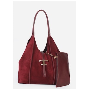 May include: A burgundy suede tote bag with a matching detachable pouch. The bag features a gold-tone metal clasp and chain detail. The handles are a darker shade of burgundy.